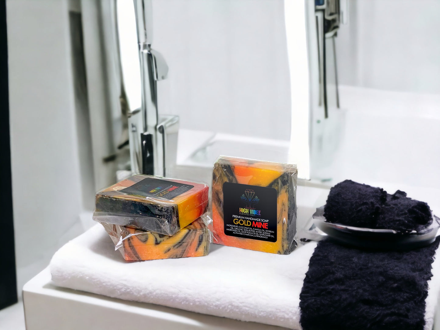 In the photo, there is the “Gold Mine” High Vibee Soap. The soap is orange, black and yellow swirls in it. The photo shows three of these soaps on top of a cloth on a beautiful bathroom counter.
