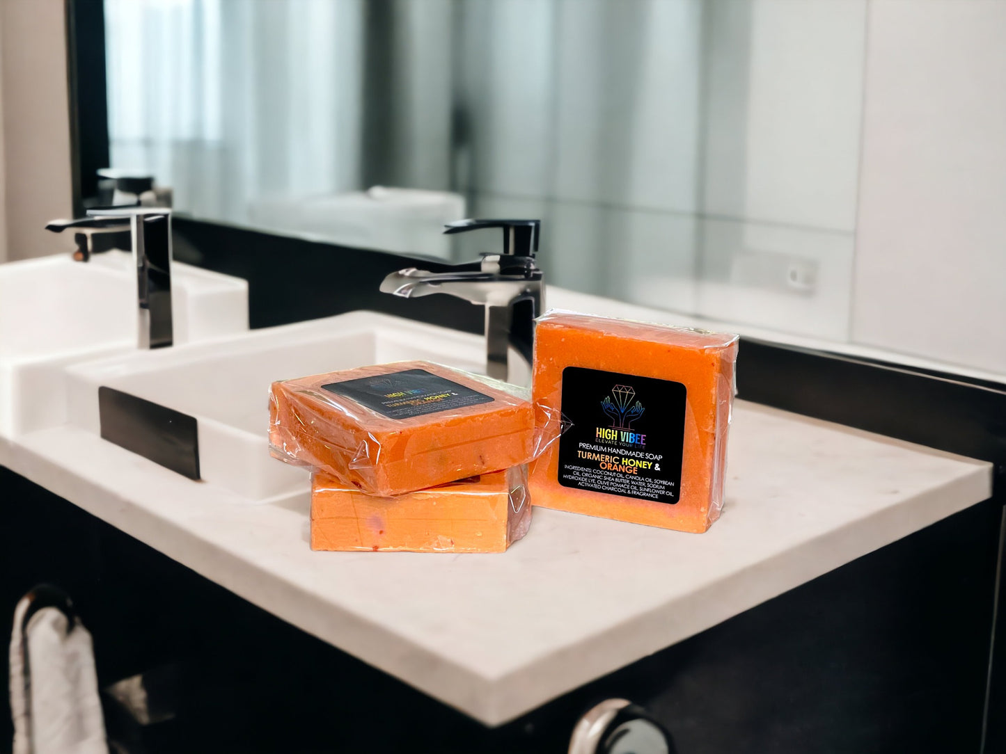 In the photo, there is the “Turmeric, Honey & Orange” High Vibee Soap. The soap is an orange color with hints of yellow. The photo shows three of these soaps on top of a cloth on a beautiful bathroom counter.