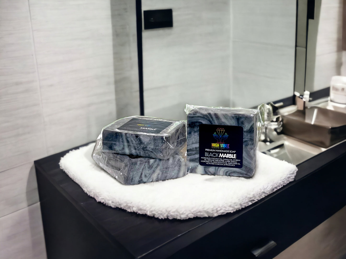 In the photo, there is the "Black Marble" High Vibee Soap. The soap has black and white swirls in it. The photo shows three of these soaps on top of a cloth on a beautiful bathroom counter.