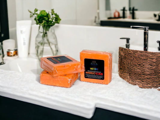 In the photo, there is the “Mango Scrub” High Vibee Soap. The soap is a bright orange. The photo shows three of these soaps on top of a cloth on a beautiful bathroom counter.