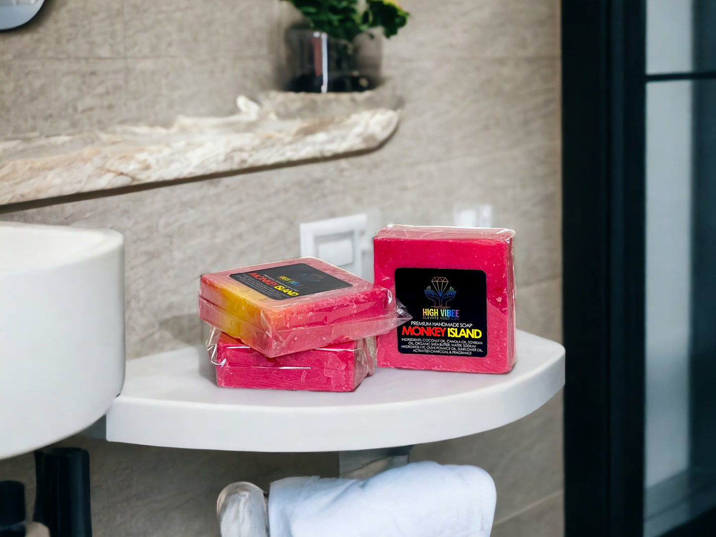 In the photo, there is the “Monkey Island” High Vibee Soap. The soap is a dark pink, with hints of yellow. The photo shows three of these soaps on top of a cloth on a beautiful bathroom counter.