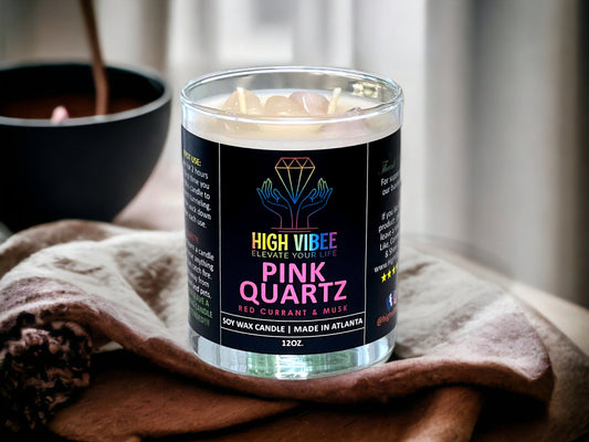 In this photo, there is a jar of High Vibee's “Pink Quartz” 12oz. Candle, scented with Red Currant & Musk. In the photo, the top is off of the candle, and there are two wicks along with clear and pink rose quartz crystals inside.