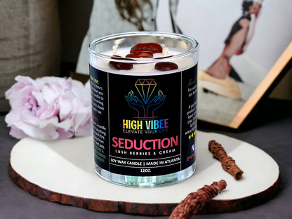 In this photo, there is a jar of High Vibee's “Seduction” 12oz. Candle, scented with Lush Berries & Cream. In the photo, the top is off of the candle, and there are two wicks along with reddish brown crystals inside.