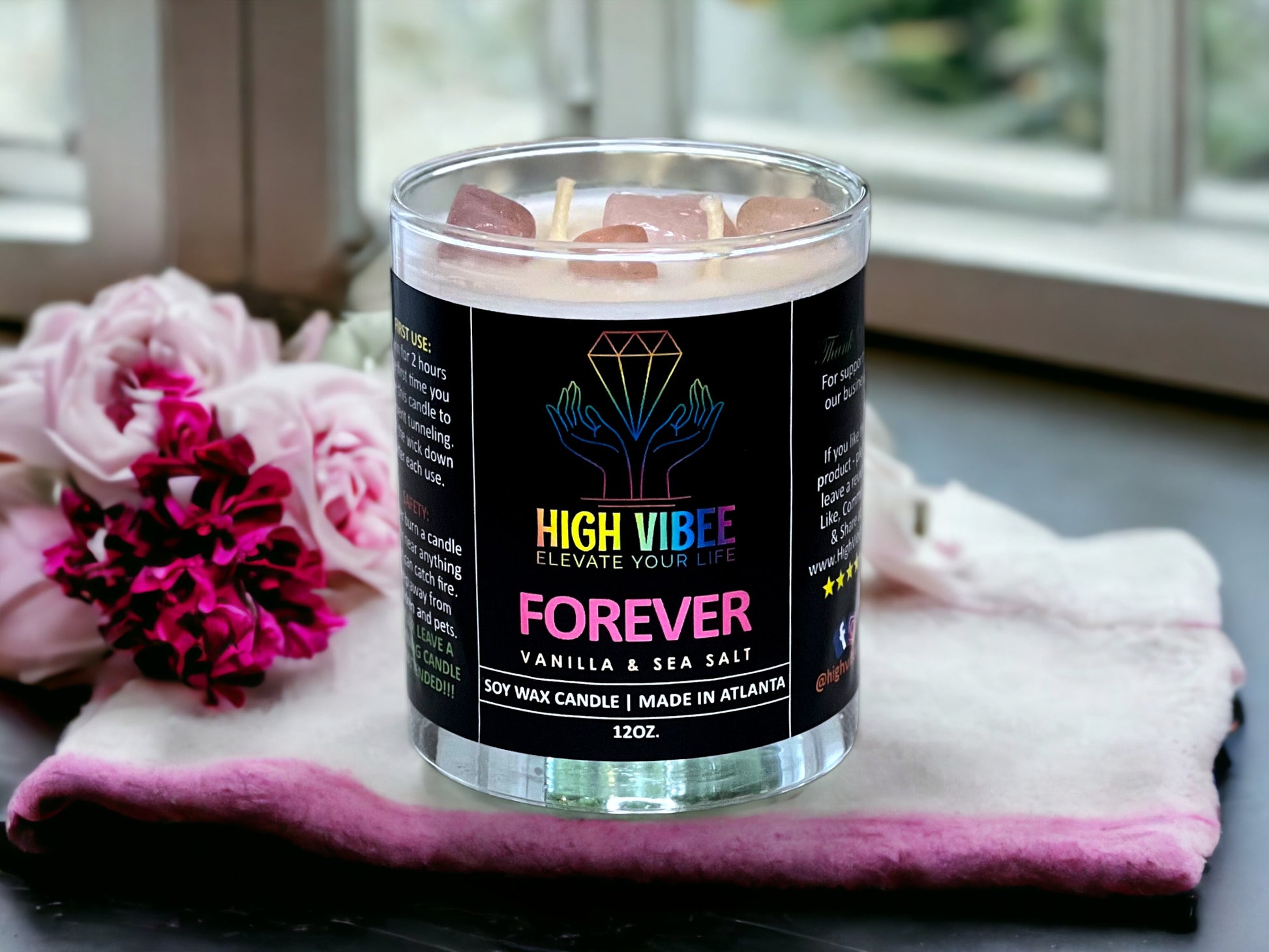 In this photo, there is a jar of High Vibee's “Forever” 12oz. Candle, scented with Vanilla & Sea Salt. In the photo, the top is off of the candle, and there are two wicks along with pink rose quart crystals inside.