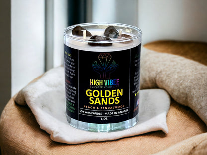 In this photo, there is a jar of High Vibee's “Golden Sands” 12oz. Candle, scented with Peach & Sandalwood. In the photo, the top is off of the candle, and there are two wicks along with brown and black crystals inside.
