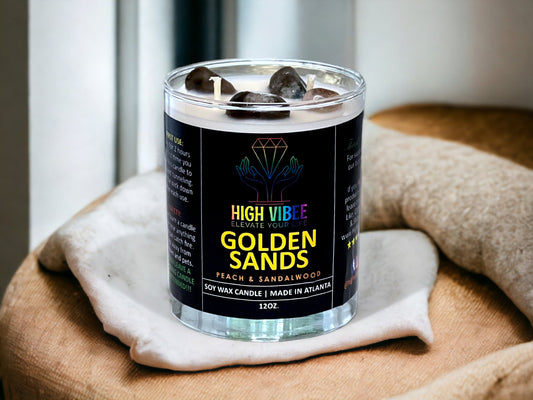 In this photo, there is a jar of High Vibee's “Golden Sands” 12oz. Candle, scented with Peach & Sandalwood. In the photo, the top is off of the candle, and there are two wicks along with brown and black crystals inside.