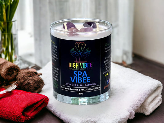 In this photo, there is a jar of High Vibee's “Spa Vibee” 12oz. Candle, scented with Lavender & Sandalwood. In the photo, the top is off of the candle, and there are two wicks along with purple crystals inside.