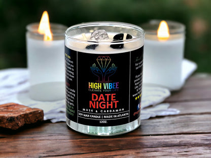 In this photo, there is a jar of High Vibee's “Date Night” 12oz. Candle, scented with Musk & Cardamon. In the photo, the top is off of the candle, and there are two wicks along with white and black crystals inside.